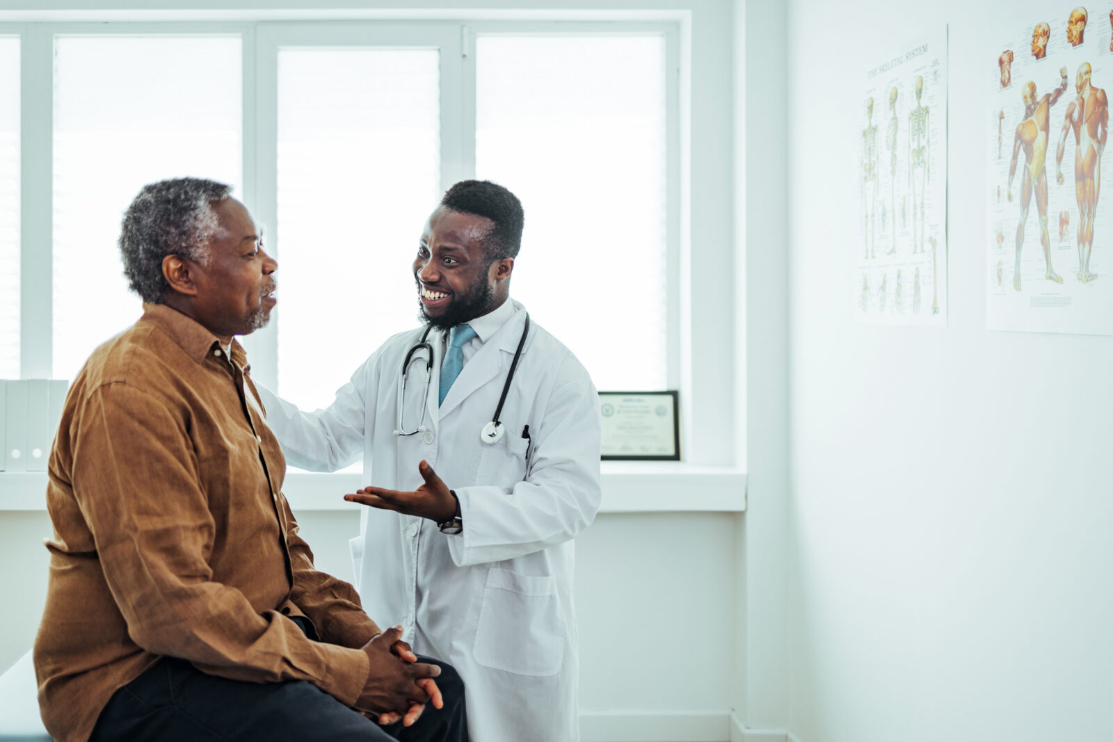 A Black male doctor chats to an elderly Black male patient.