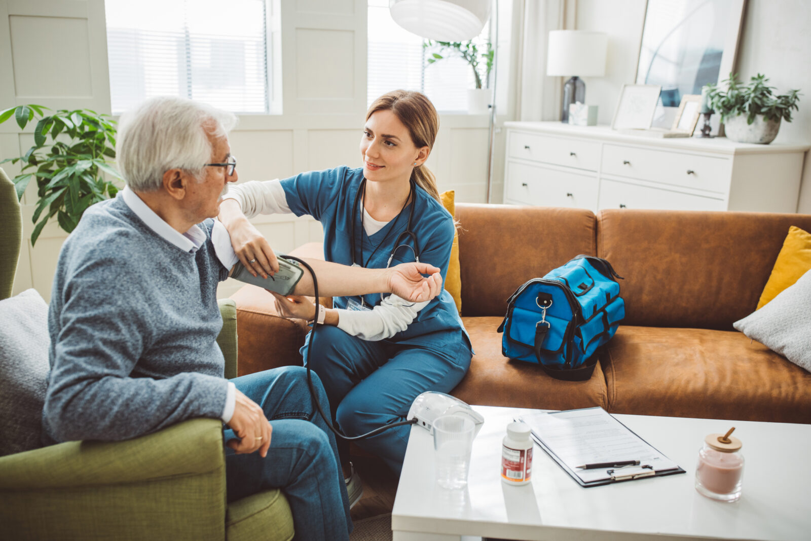 Home health care provider visiting a mature male patient at home. She is measuring blood pressure to patient at his living room.